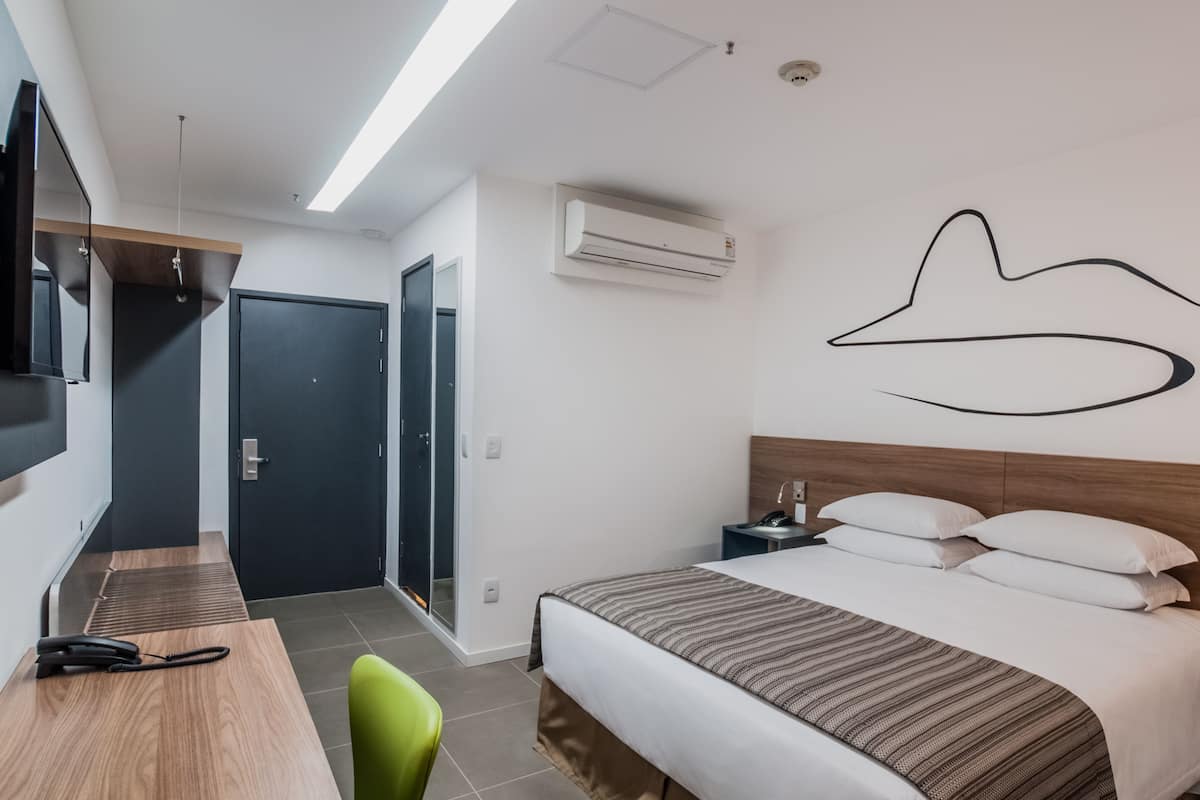 Una habitación de hotel moderna con cama, escritorio, silla, televisión, aire acondicionado y una puerta.
