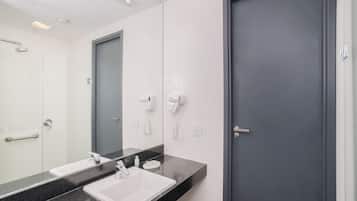 Un baño moderno con un lavabo de superficie negra, un espejo y dos secadores de pelo montados en la pared.