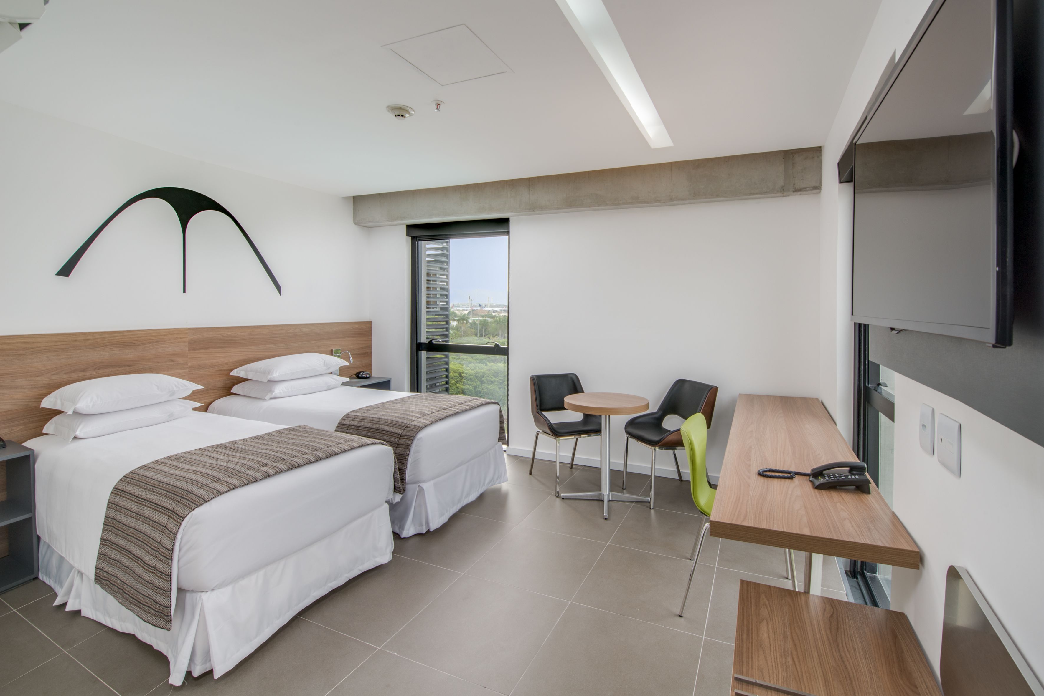 A hotel room with two beds, a small table with chairs, a TV, and a window with a view.
