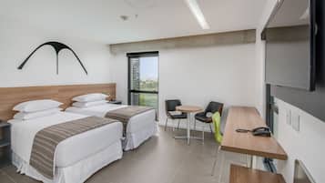 A hotel room with two beds, a small table with chairs, a TV, and a window with a view.