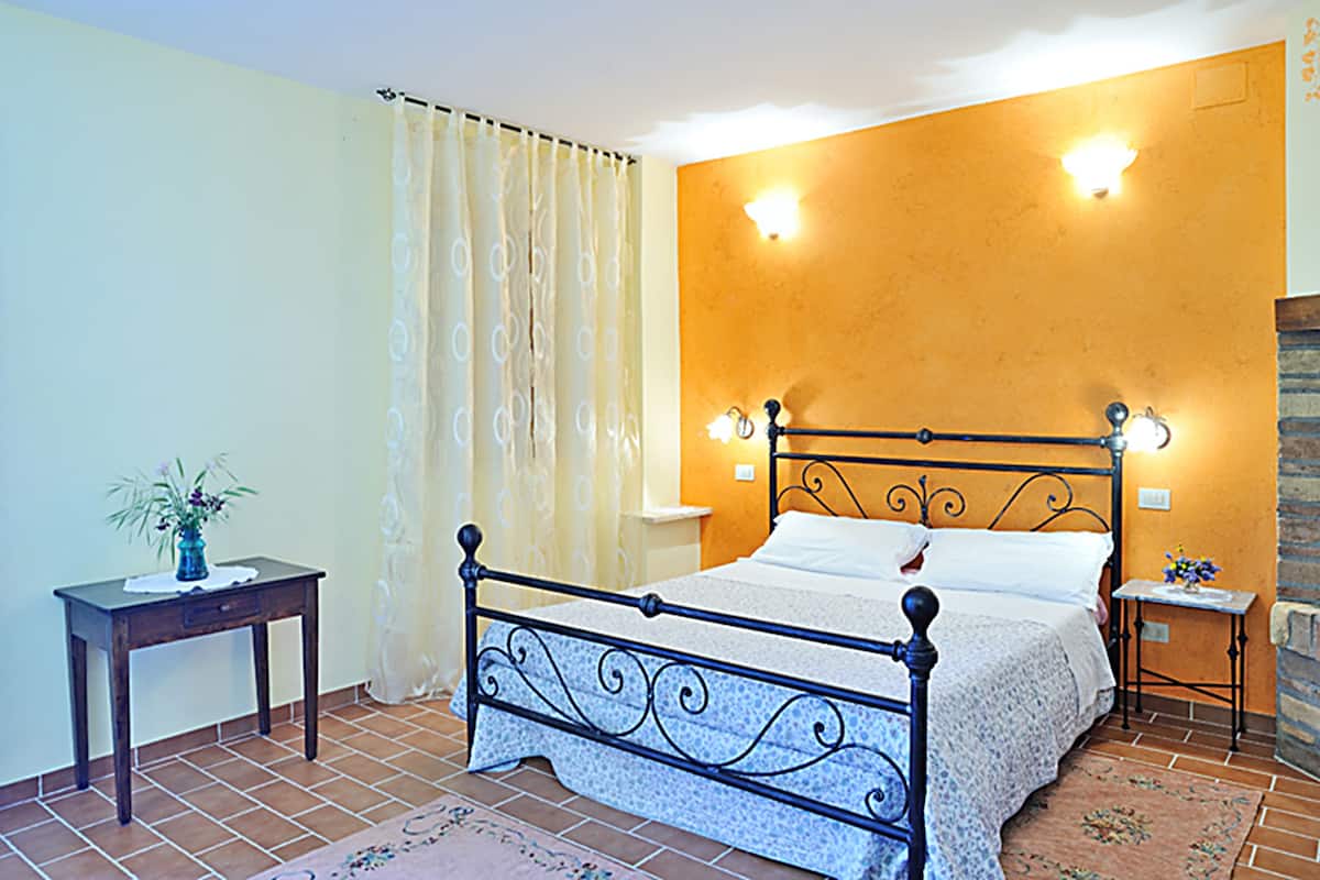 Une chambre à coucher avec un lit, une table de chevet, une petite table sur laquelle se trouve un vase, et un rideau.