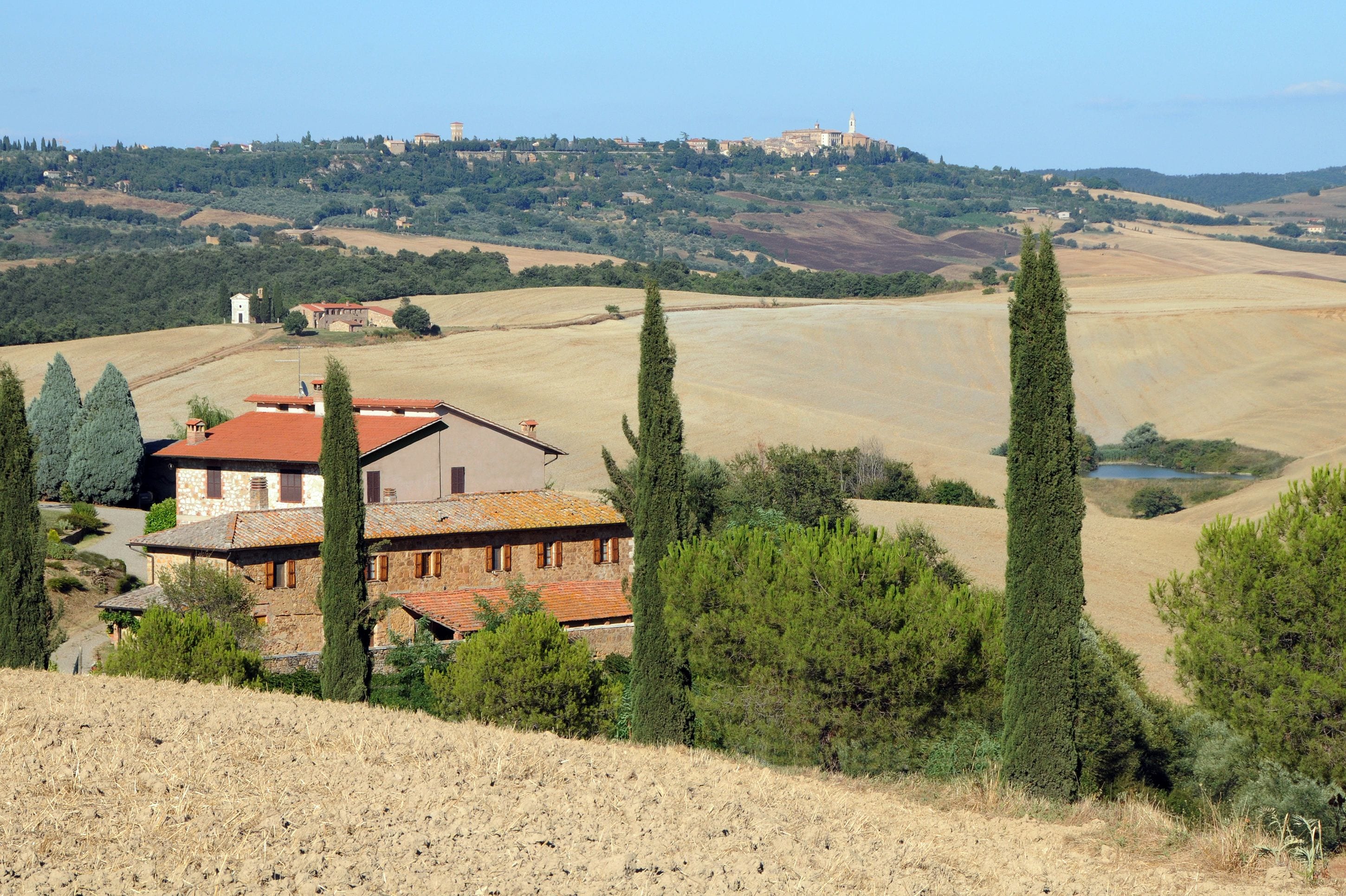 A rural house with a red roof, surrounded by trees and fields.