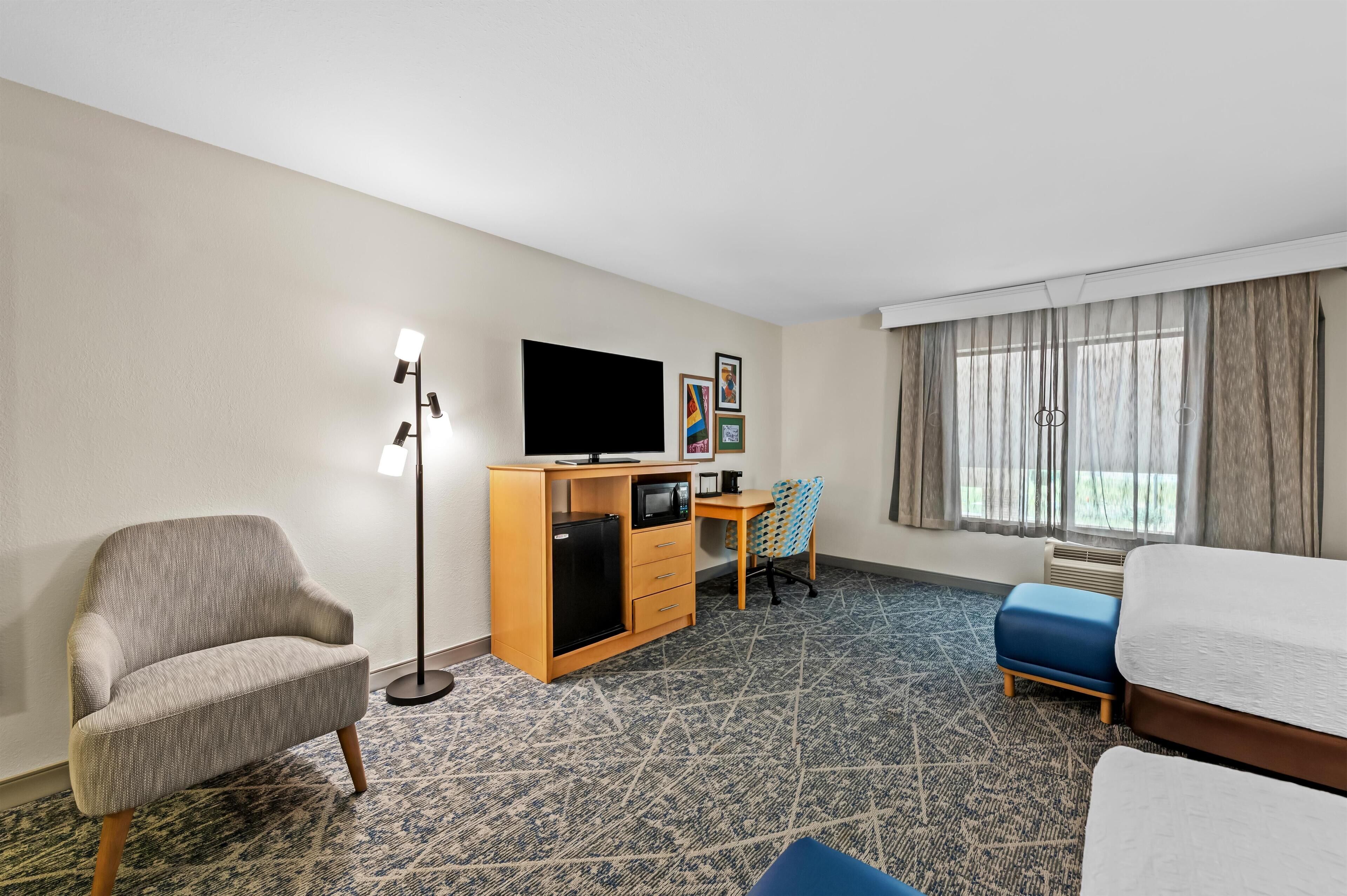 Una habitación de hotel con sofá, escritorio, computadora, televisor y cama.