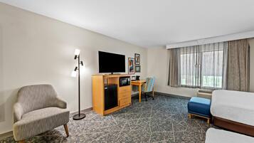 Una habitación de hotel con sofá, escritorio, computadora, televisor y cama.