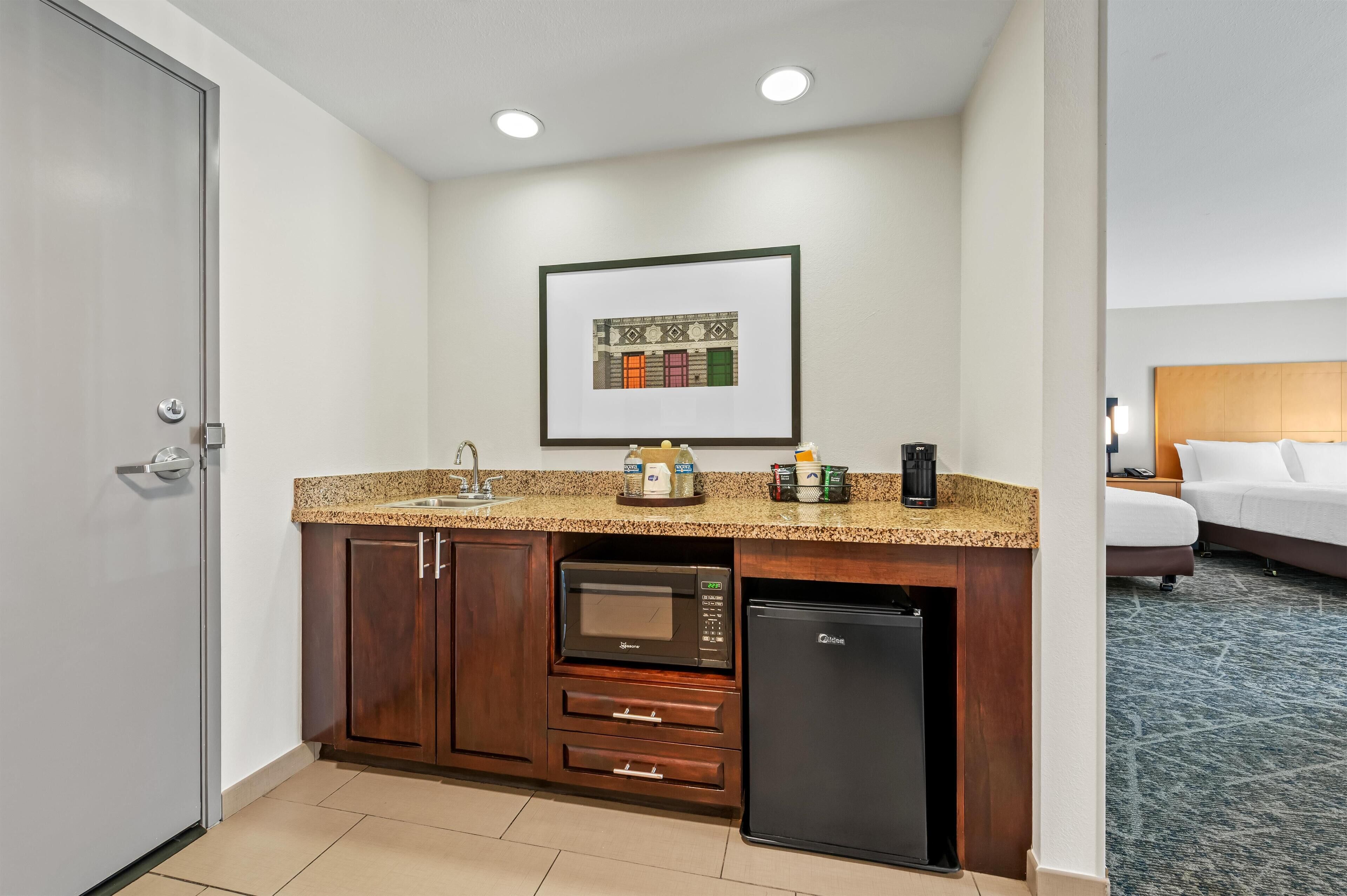 A compact hotel kitchen with a microwave, refrigerator, and a framed picture on the wall.
