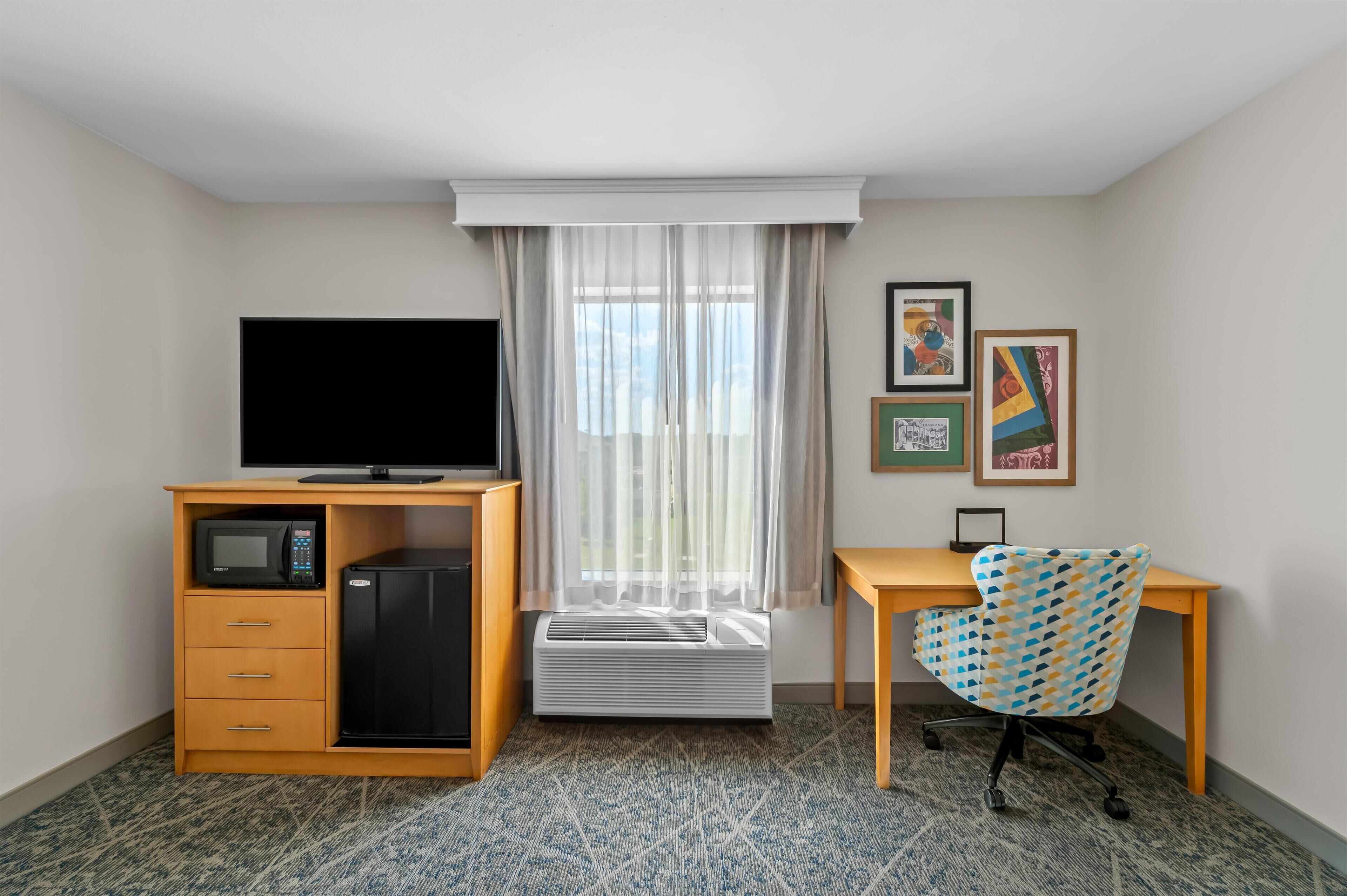 Habitación de hotel con escritorio, silla, televisión, microondas y aire acondicionado.