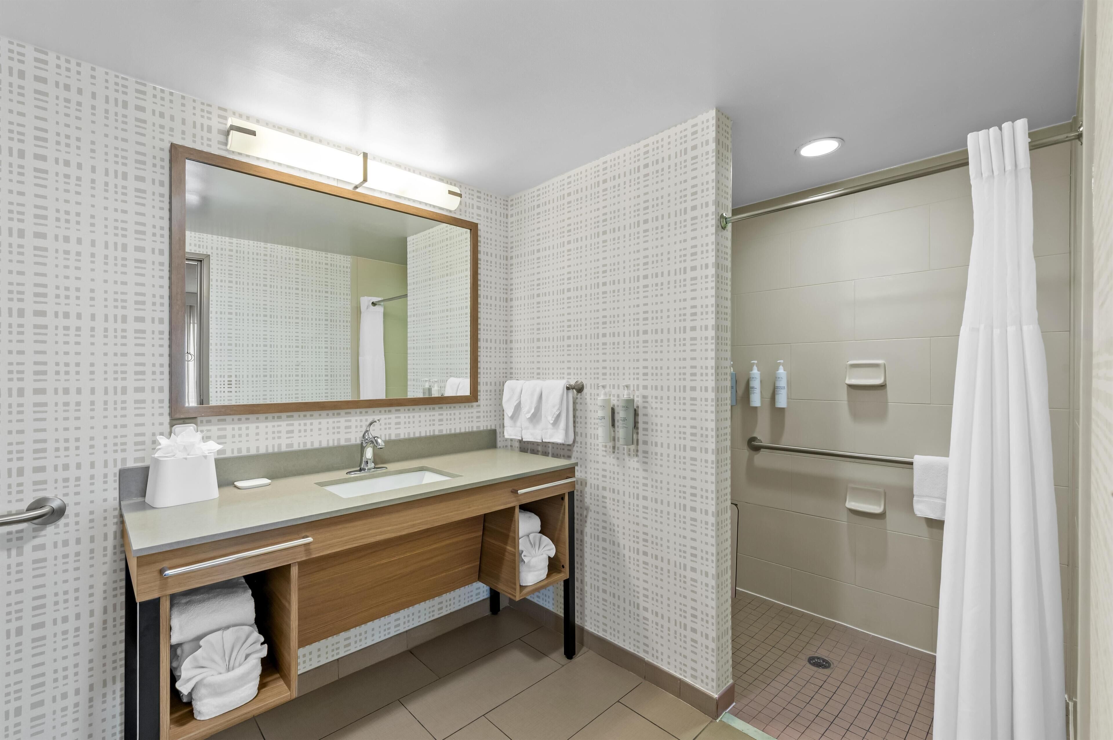 A modern bathroom with a large mirror, a sink, a shower, and a towel rack.