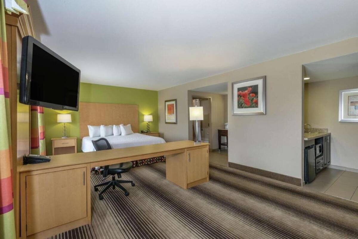 A hotel room with a bed, desk, television, and a small kitchenette.