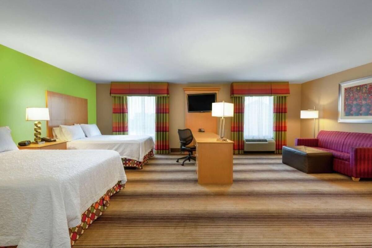 A hotel room with two beds, a desk, a sofa, and a TV.