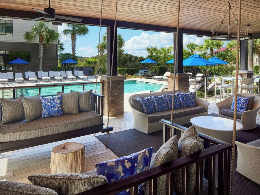 A poolside area with a swing chair, sofas, and umbrellas.
