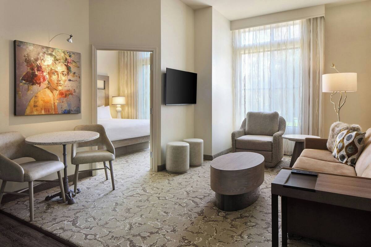 A hotel room with a bed, a TV, a sofa, a coffee table, and a painting on the wall.