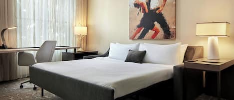 A hotel room with a large bed, a desk with a chair, two bedside lamps, and a painting on the wall.