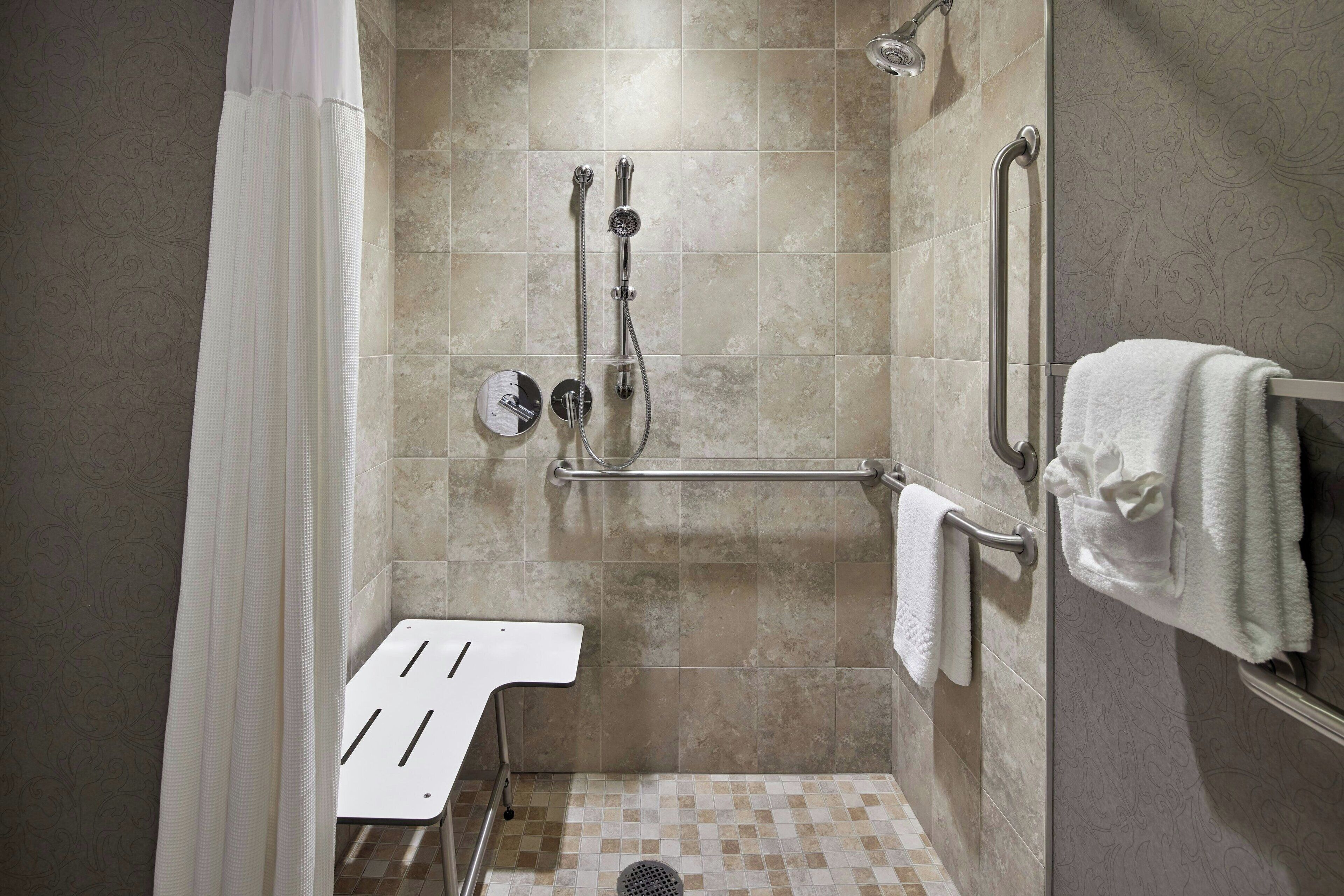 A shower area with a grab bar, a white towel rack, and a showerhead.