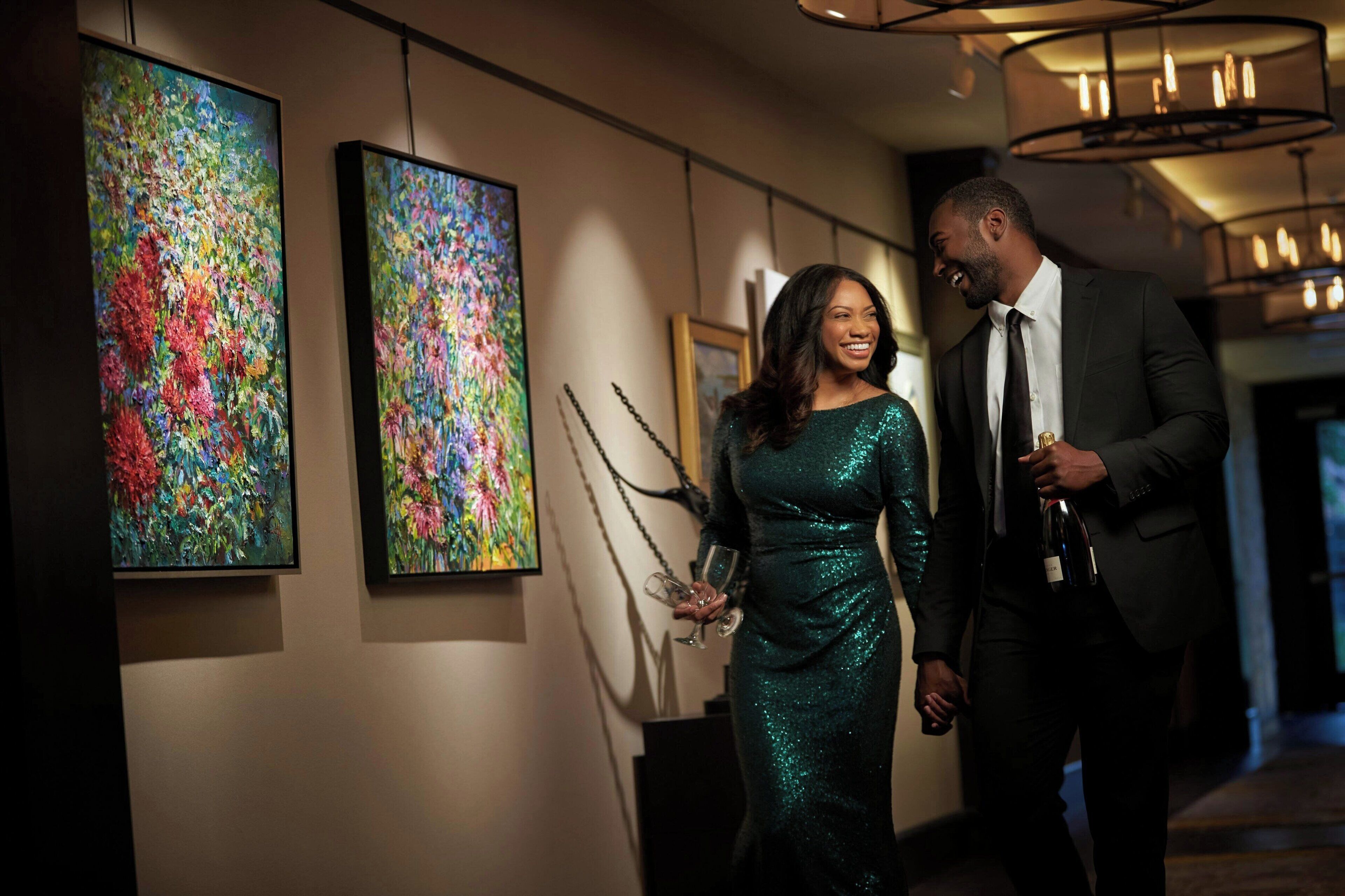 A couple walking through a hallway with abstract paintings on the walls.