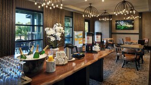 Un espace d’accueil d’hôtel comprenant un bar, des sièges et une grande fenêtre donnant sur des palmiers.