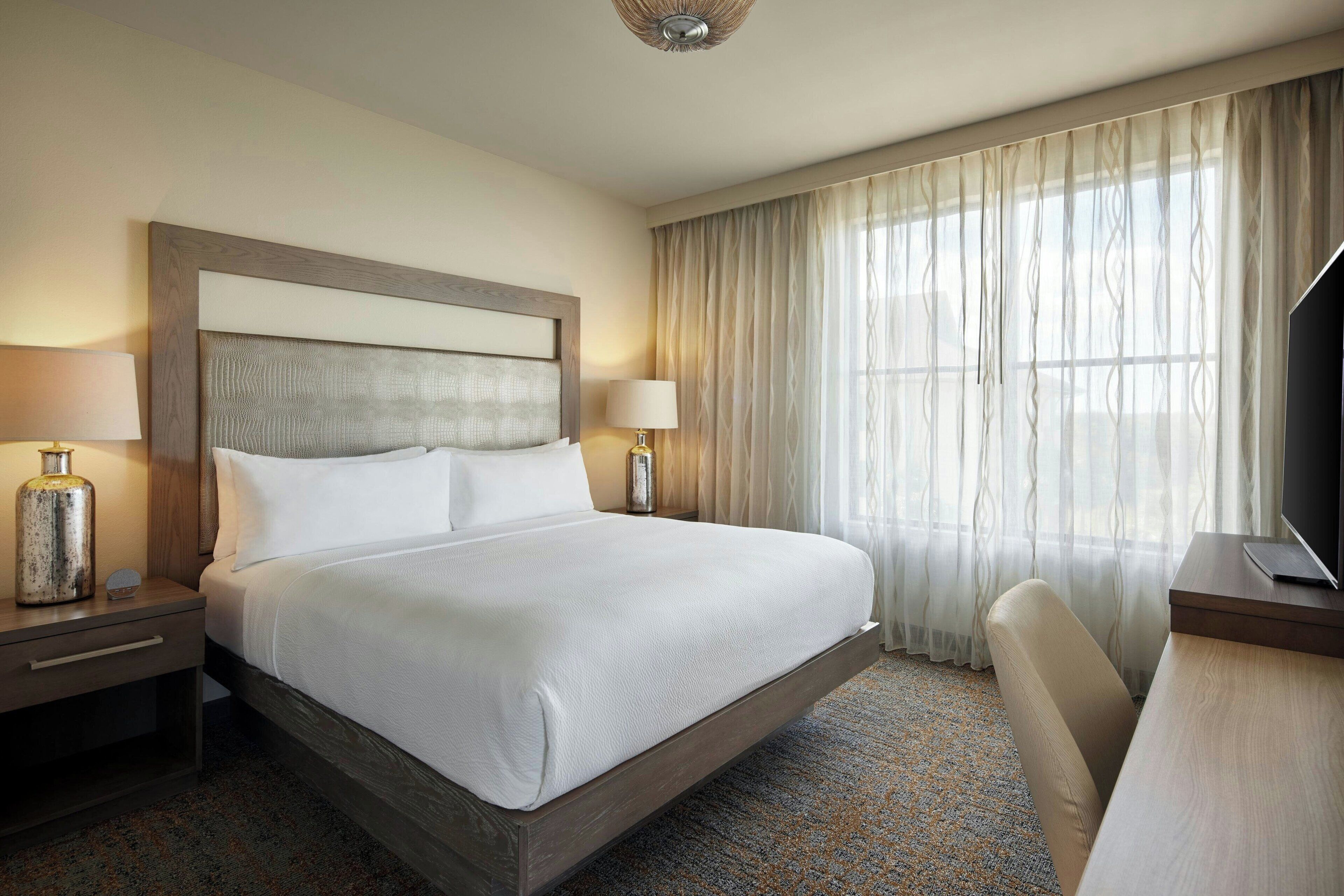 A hotel room with a large bed, two bedside tables with lamps, a desk, and a TV.