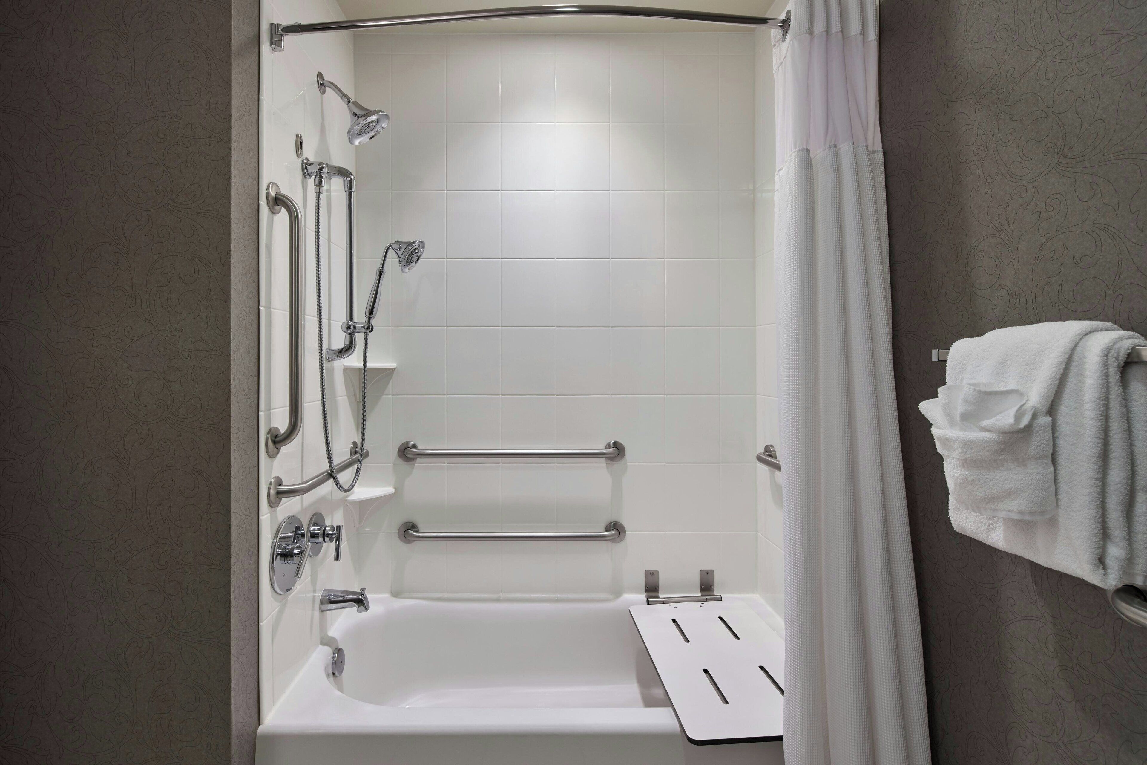 Une salle de bain moderne équipée d’une baignoire, de barres d’appui et d’un pommeau de douche.