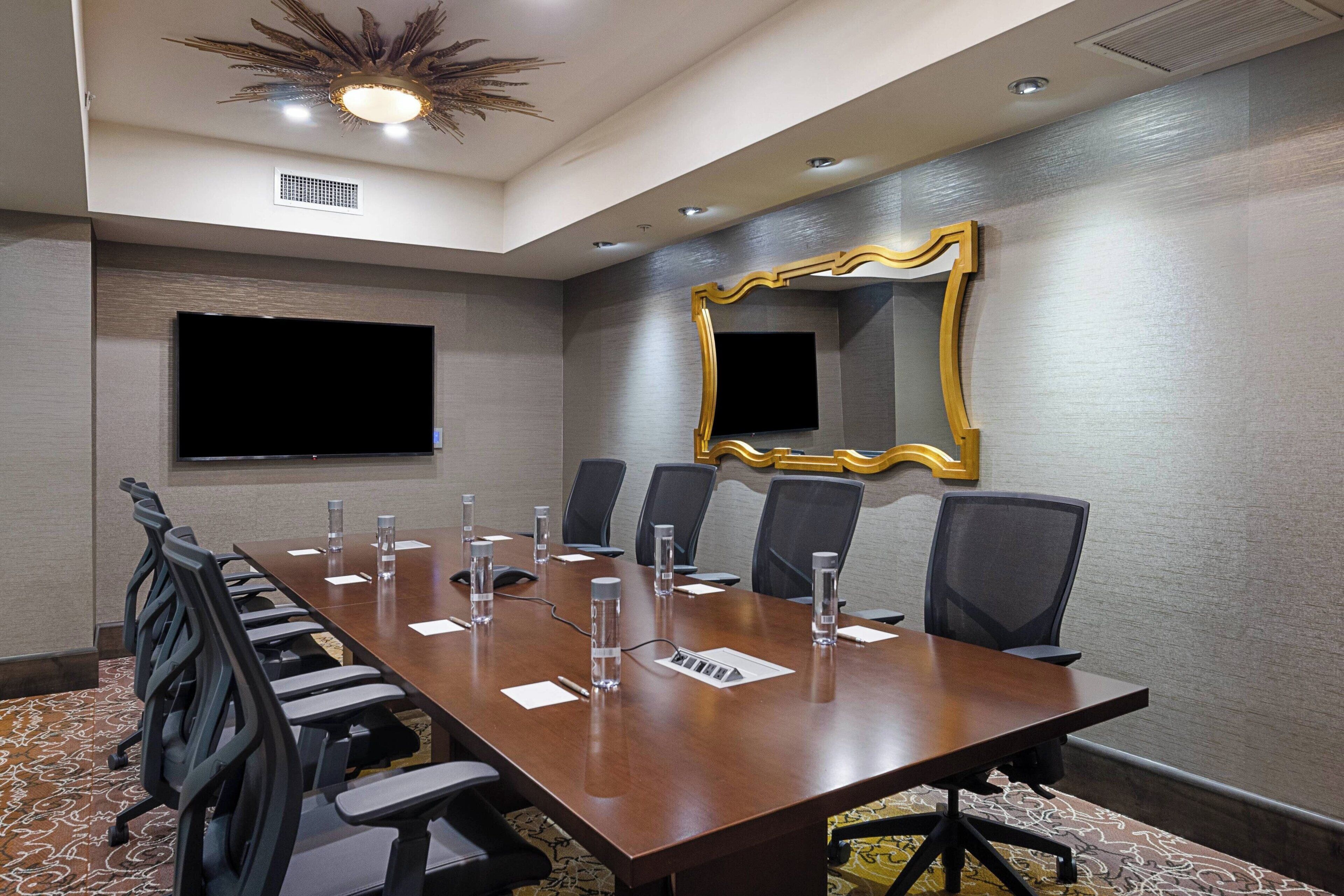 A conference room with a long table, chairs, a television, and a decorative mirror.