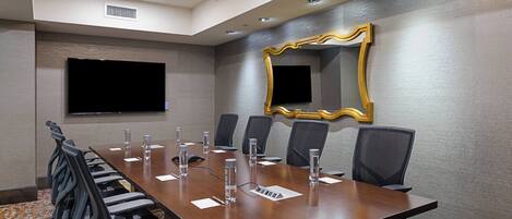 A conference room with a long table, chairs, a television, and a decorative mirror.