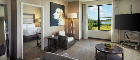 Habitación de hotel con cama, sofá, sillón, televisor, lámpara y vistas al exterior.