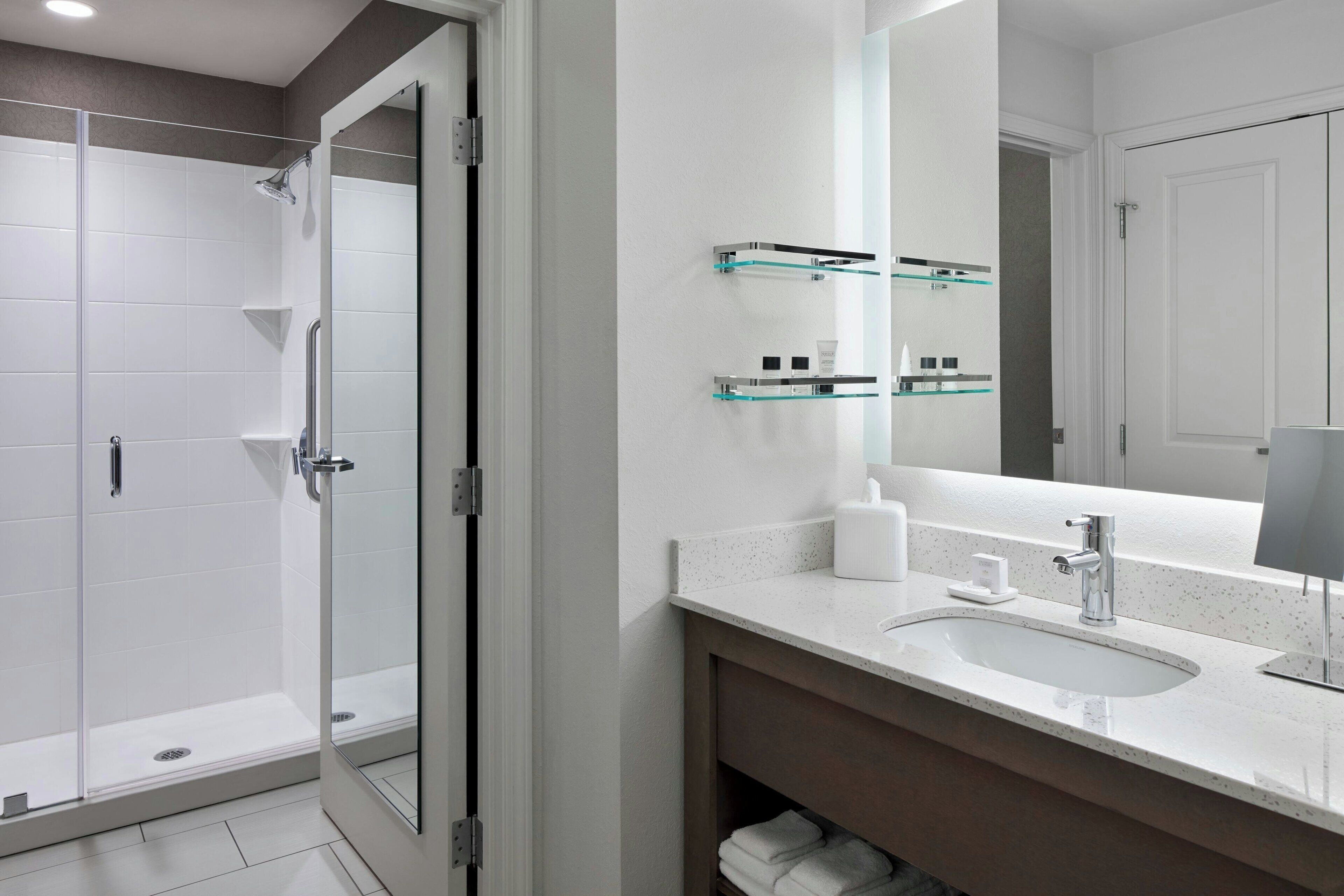 A modern bathroom with a glass shower enclosure, a sink with a mirror, and glass shelves above the sink.