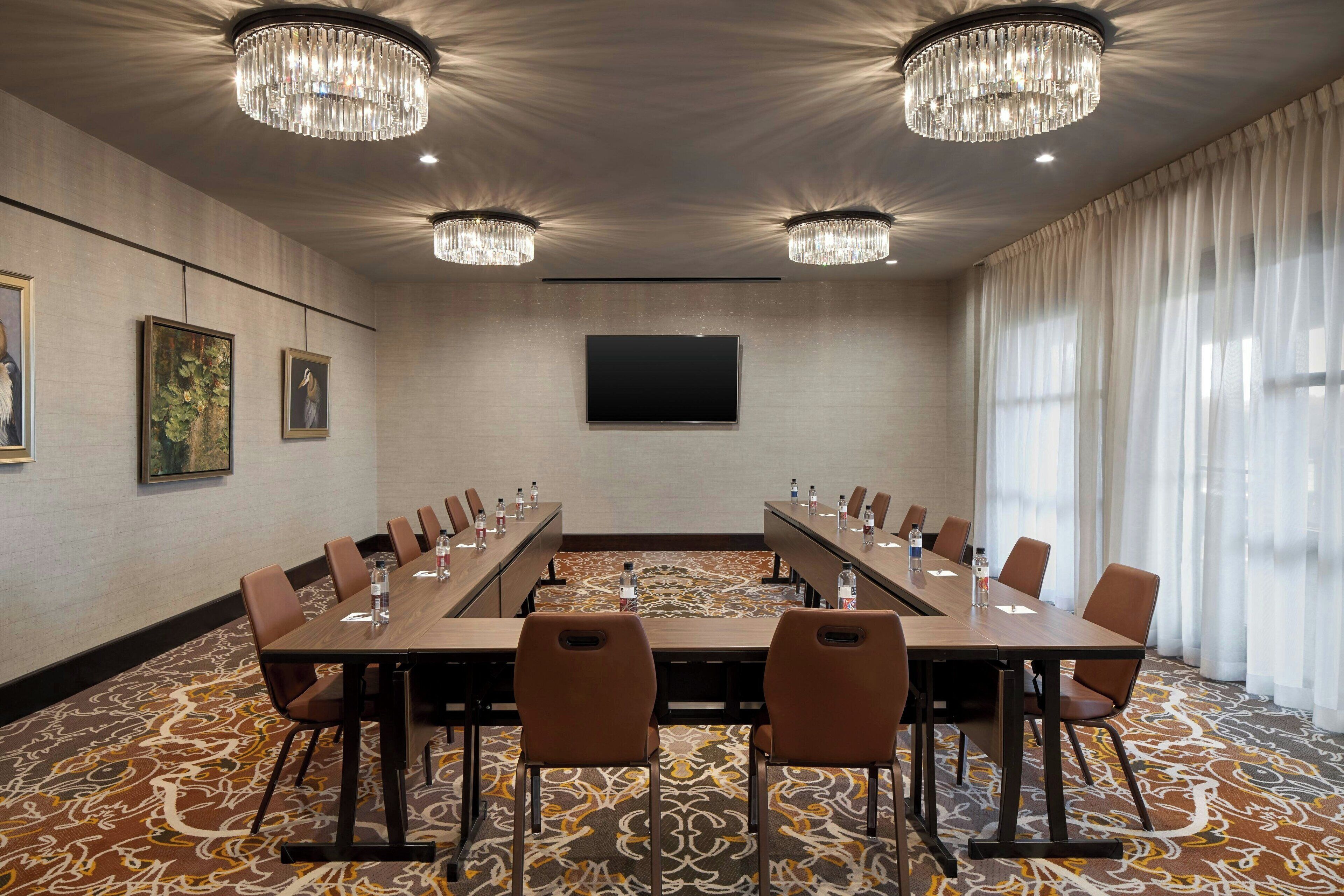 A conference room with a long table, chairs, a flat-screen TV, and chandeliers.