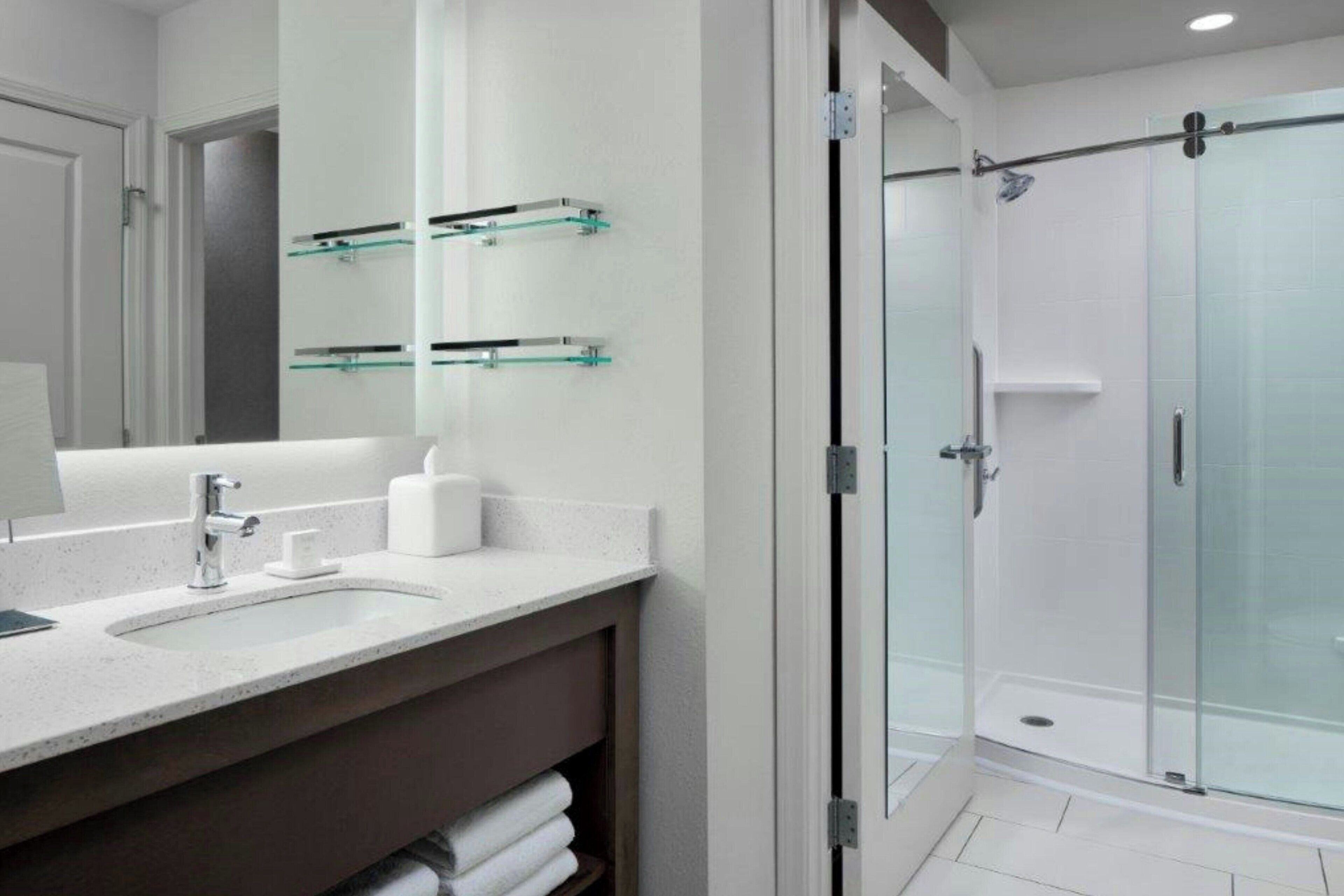 Een moderne badkamer met een douchecabine van glas, een grote spiegel en een aanrecht met een wastafel en toiletartikelen.