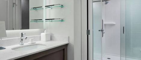Een moderne badkamer met een douchecabine van glas, een grote spiegel en een aanrecht met een wastafel en toiletartikelen.