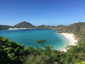 Un paisaje costero con mar azul cristalino, playa arenosa y colinas verdes exuberantes.