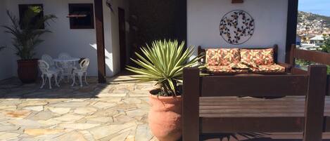 A patio with stone flooring, a wooden bench, a potted plant, and a white wall with a circular floral design.