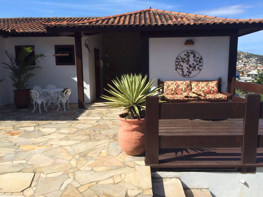 A patio with stone flooring, a wooden bench, a potted plant, and a white wall with a circular floral design.