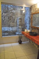 Un baño con pared de piedra, un lavamanos rojo y un ventanal grande.