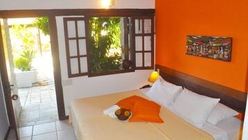 A hotel room with a bed, a window with a view of greenery, and a painting on the wall.