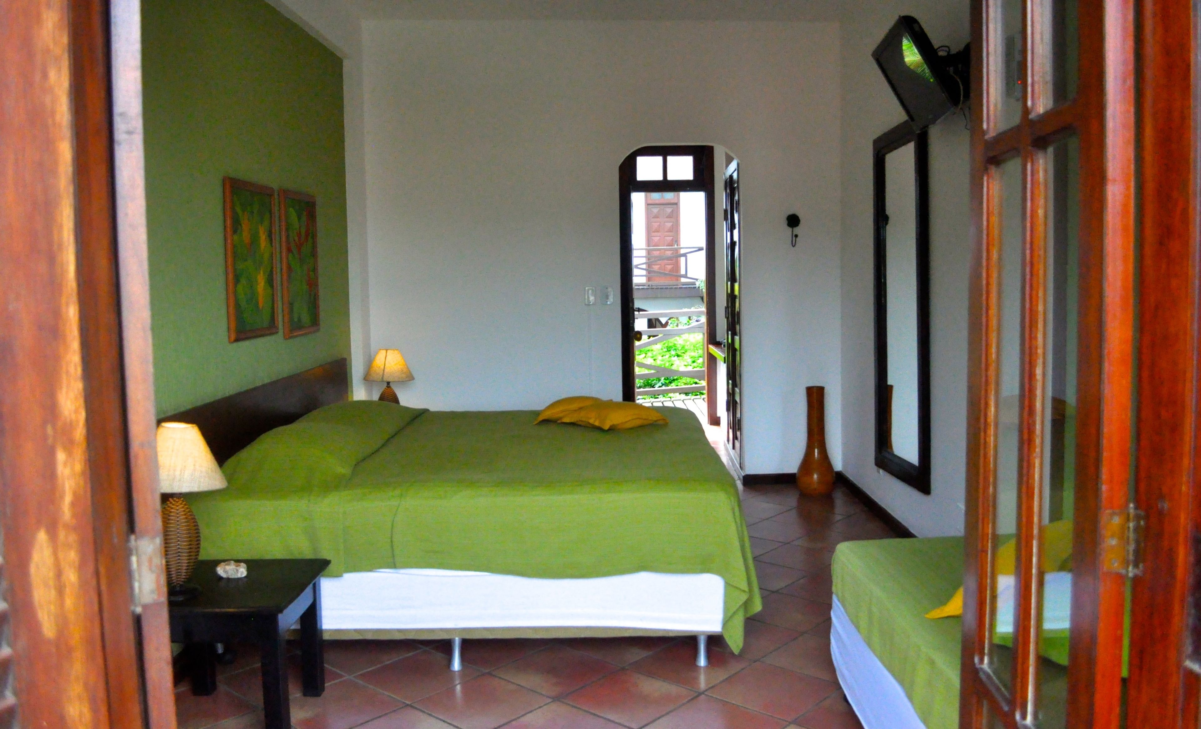 A room with a bed, a bedside table with a lamp, a window, and a door leading outside.