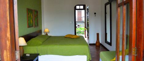 A room with a bed, a bedside table with a lamp, a window, and a door leading outside.