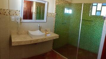 Un bagno con un lavandino color beige, uno specchio e una doccia rivestita di mosaici verdi.