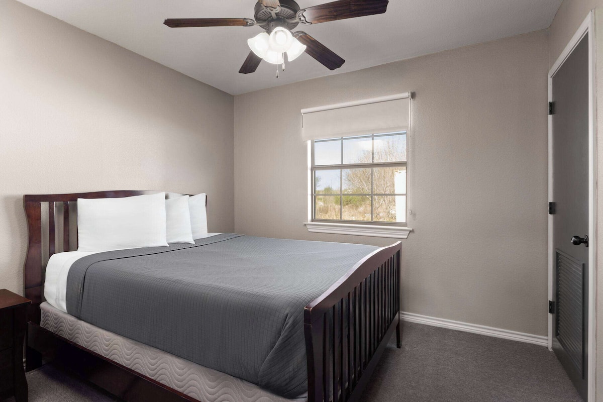 Une chambre à coucher avec un lit, un ventilateur de plafond, une fenêtre avec des stores et un radiateur.