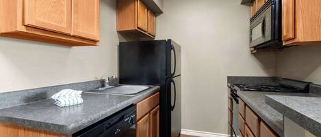 A compact kitchen with wooden cabinets, a black refrigerator, a microwave, and a dishwasher.