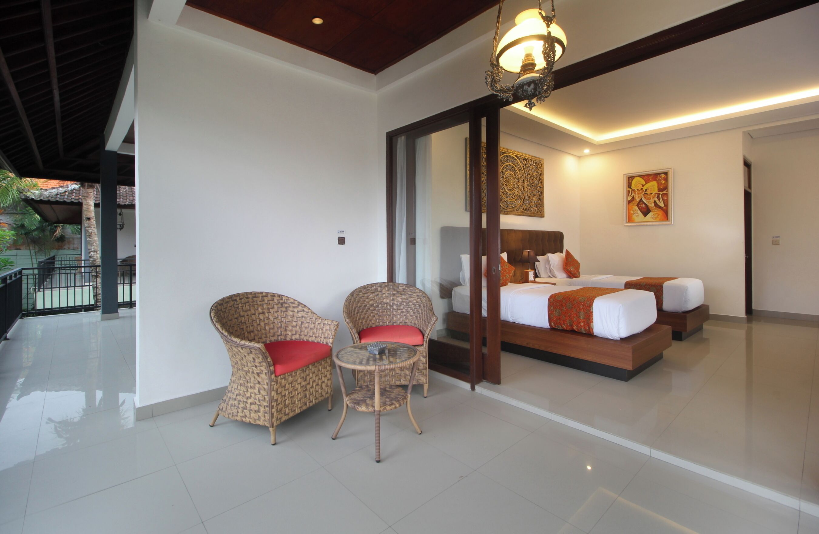 A hotel room with a bed, two wicker chairs, a small table, and a ceiling light.