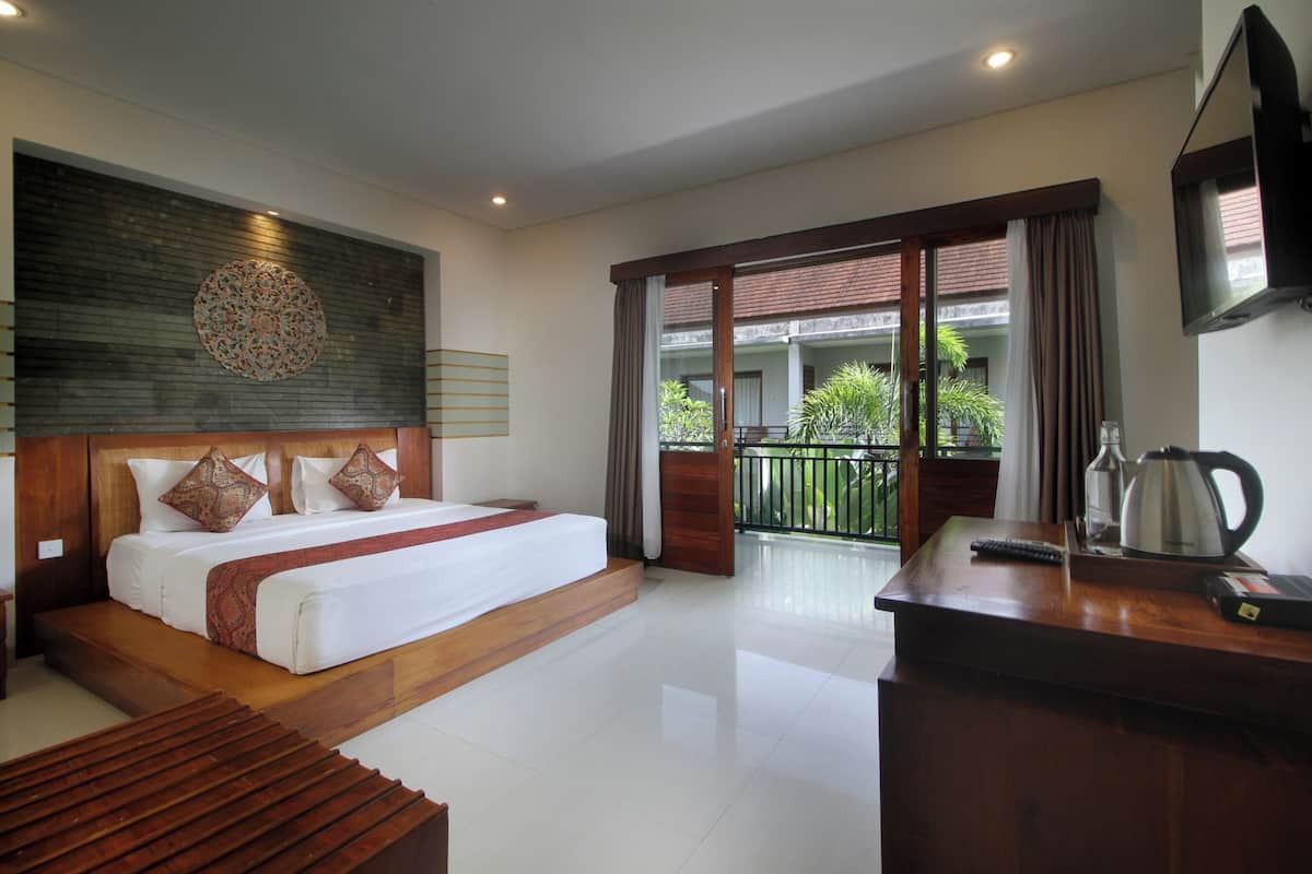 A modern hotel room with a large bed, a wooden headboard, a balcony with a view, and a coffee maker on the desk.