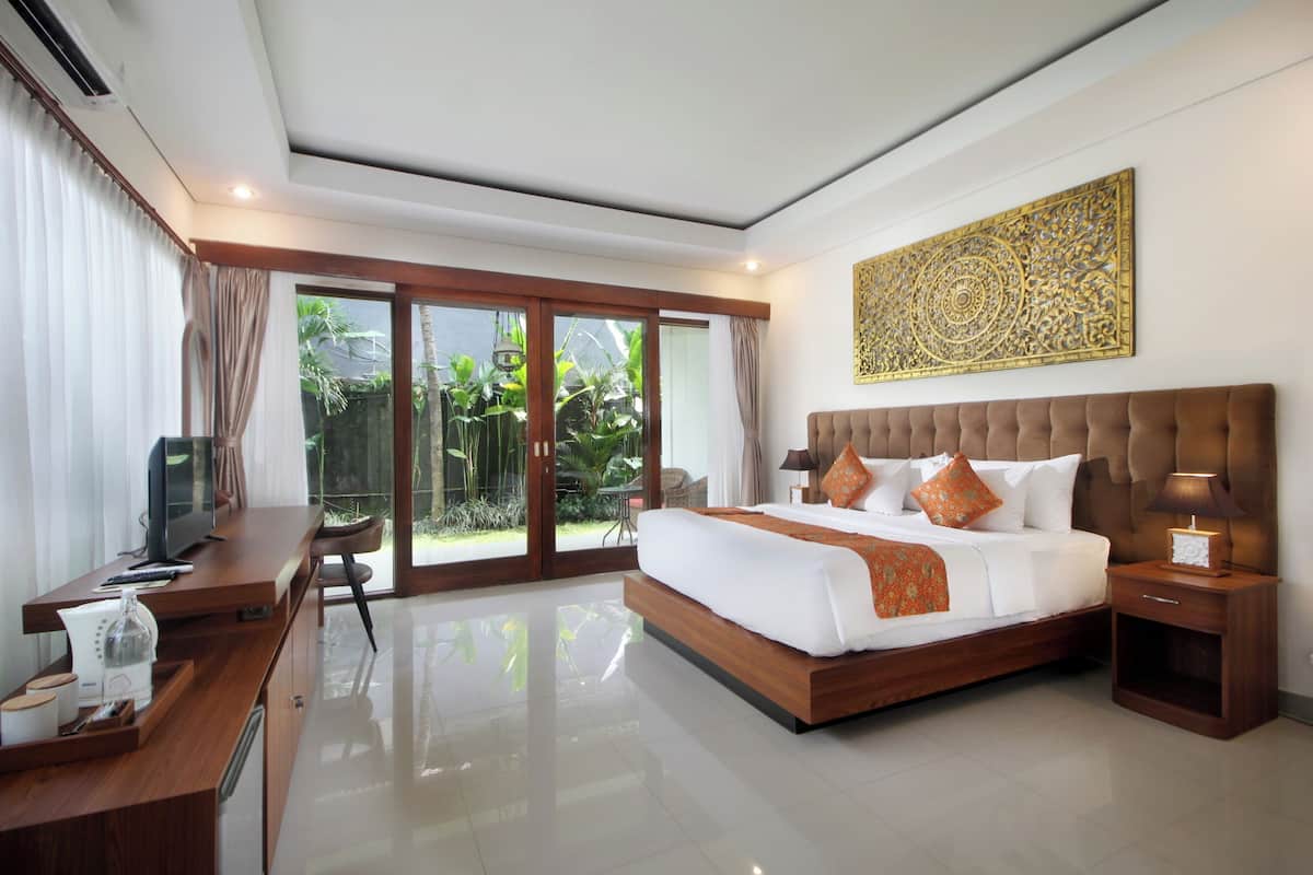 A modern bedroom with a large bed, a desk with a TV, and a view of greenery through the sliding glass doors.