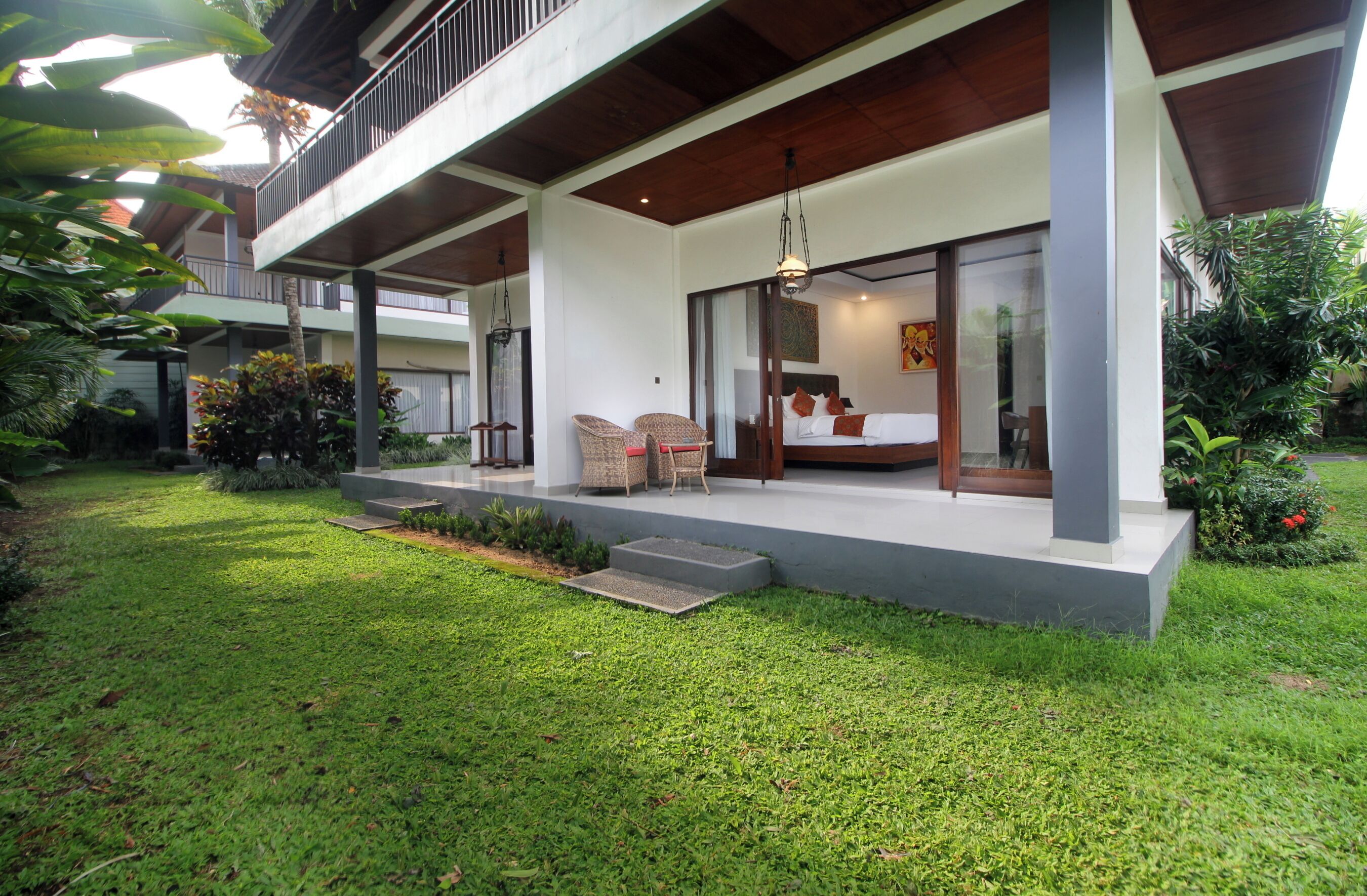 A modern hotel with a covered outdoor seating area, a balcony, and a well-maintained garden.