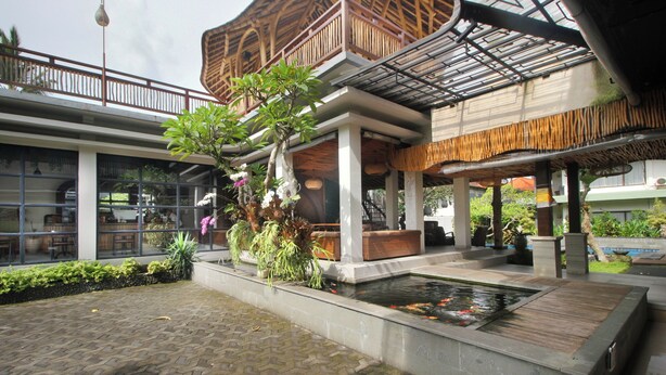 Un espace extérieur abrité doté d’un élément décoratif aquatique, de sièges et d’un bâtiment avec un balcon en bois.