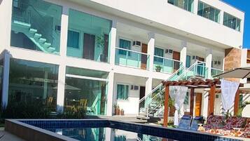 Um edifício moderno com piscina, fachada de vidro e área externa com mesas e cadeiras.