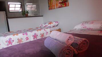 Un dormitorio con dos camas, cada una con ropa de cama floral, una alfombra púrpura y una toalla enrollada en el suelo.