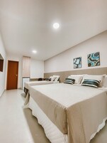 Quarto com duas camas, uma escrivaninha e duas pinturas na parede.