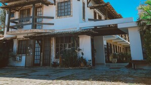A two-story building with a tiled roof, large windows, and a covered entrance area with potted plants. - Pousada Caminho Do Mar (Cabo Frio)