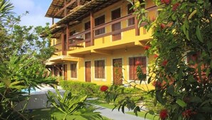 A multi-story building with balconies, surrounded by lush greenery and a pathway leading to a pool. - Pousada Caminho Do Mar (Cabo Frio)