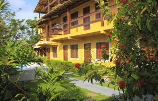 Um edifício de vários andares com varandas, cercado por vegetação exuberante e um caminho que leva a uma piscina.