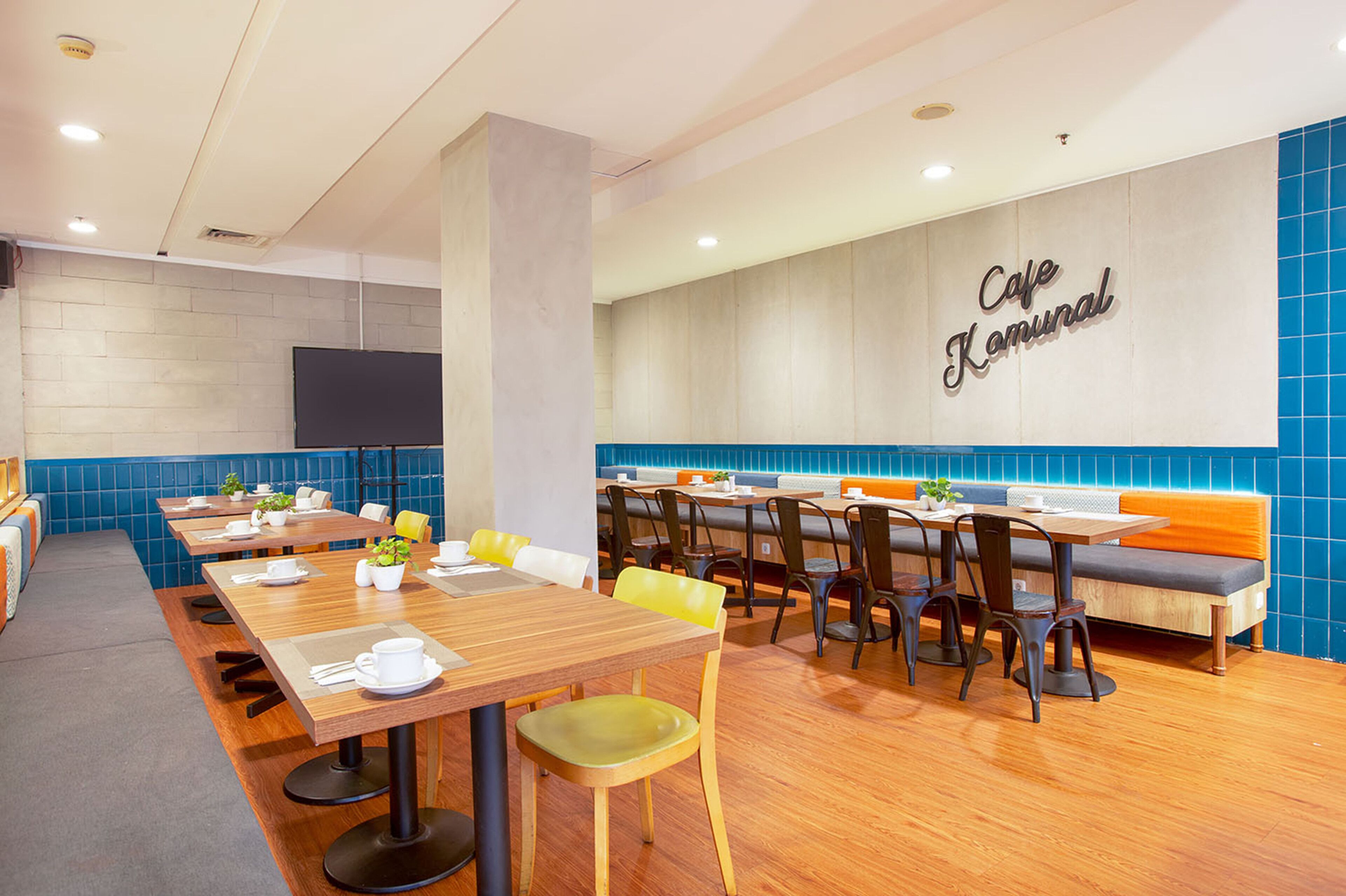 Un café moderne avec des tables en bois, des sièges confortables et un mur recouvert de carreaux bleus sur lequel est inscrit le nom du café.